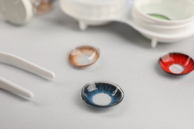 Photo of Different color contact lenses and tweezers on light background, closeup