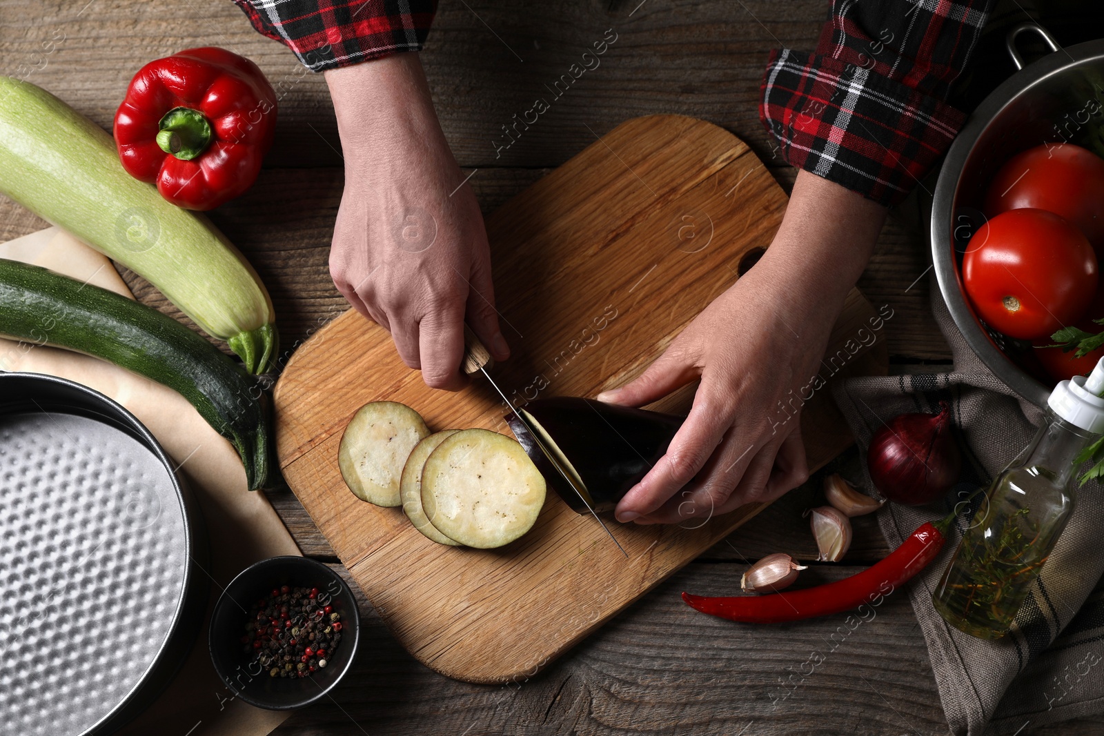 Photo of Cooking delicious ratatouille. Woman cutting fresh eggplant at wooden table, top view