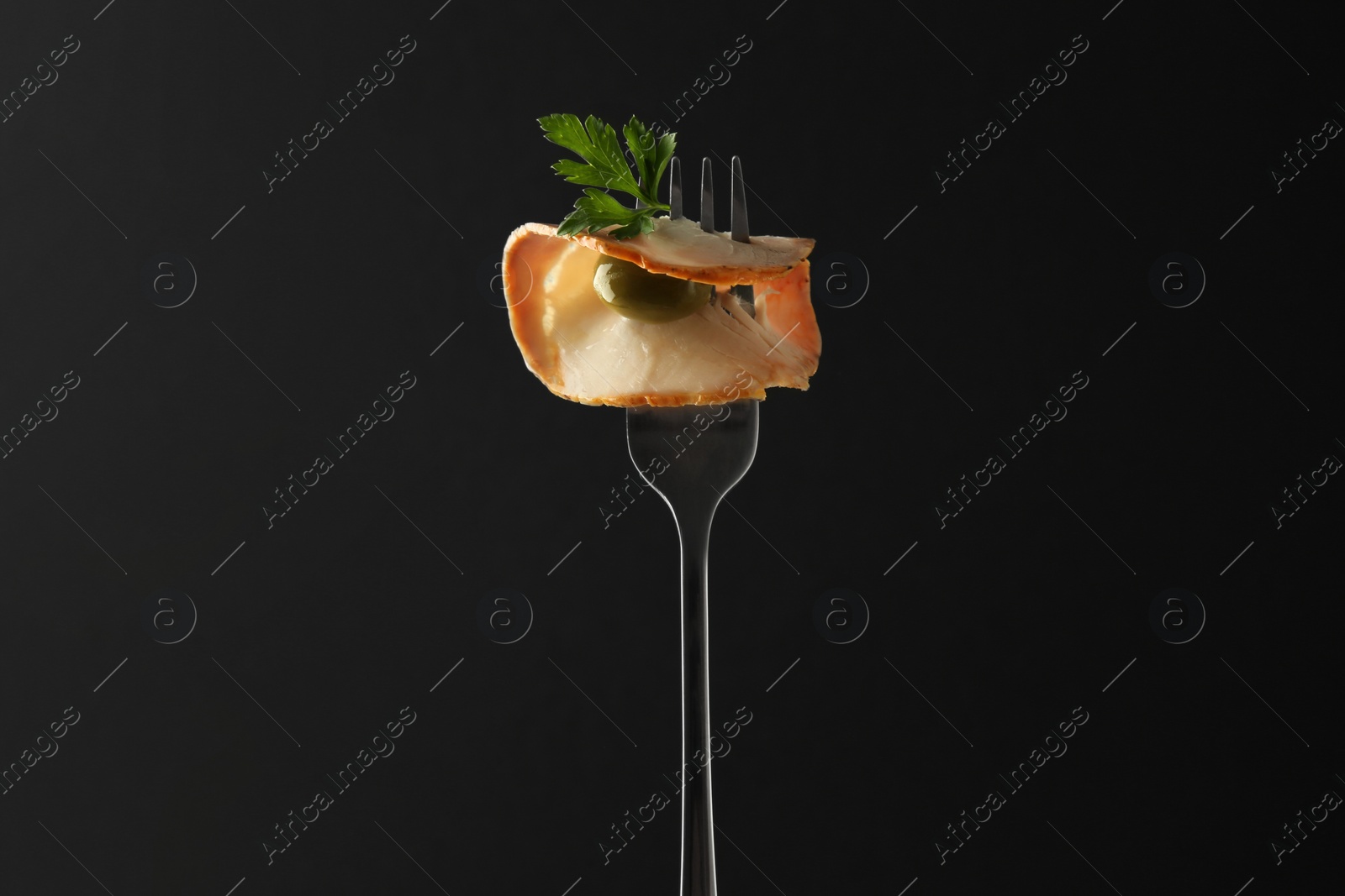 Photo of Fork with slice of ham, olive and parsley on black background