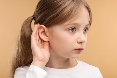 Little girl with hearing problem on pale brown background