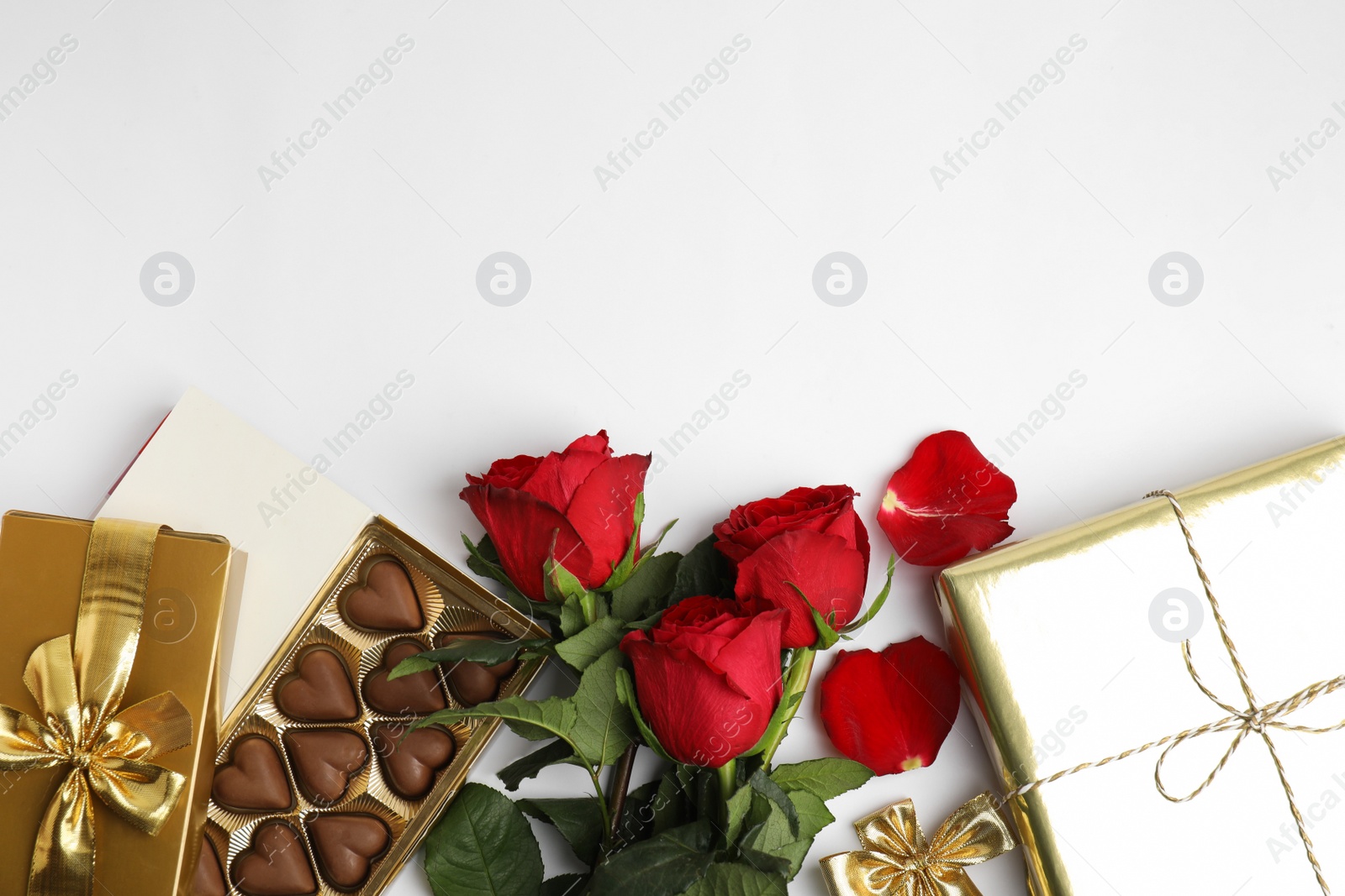 Photo of Heart shaped chocolate candies, roses and gift boxes on white background, top view. Valentine's day celebration