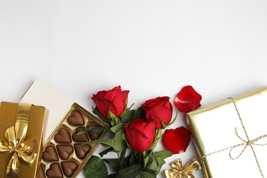 Photo of Heart shaped chocolate candies, roses and gift boxes on white background, top view. Valentine's day celebration
