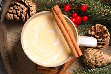 Photo of Tasty eggnog, cinnamon sticks and fir branches on wooden tray, flat lay