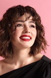 Portrait of beautiful young woman with wavy hairstyle on pink background