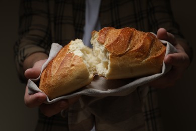 Photo of Man breaking loaf of fresh bread on dark background, closeup