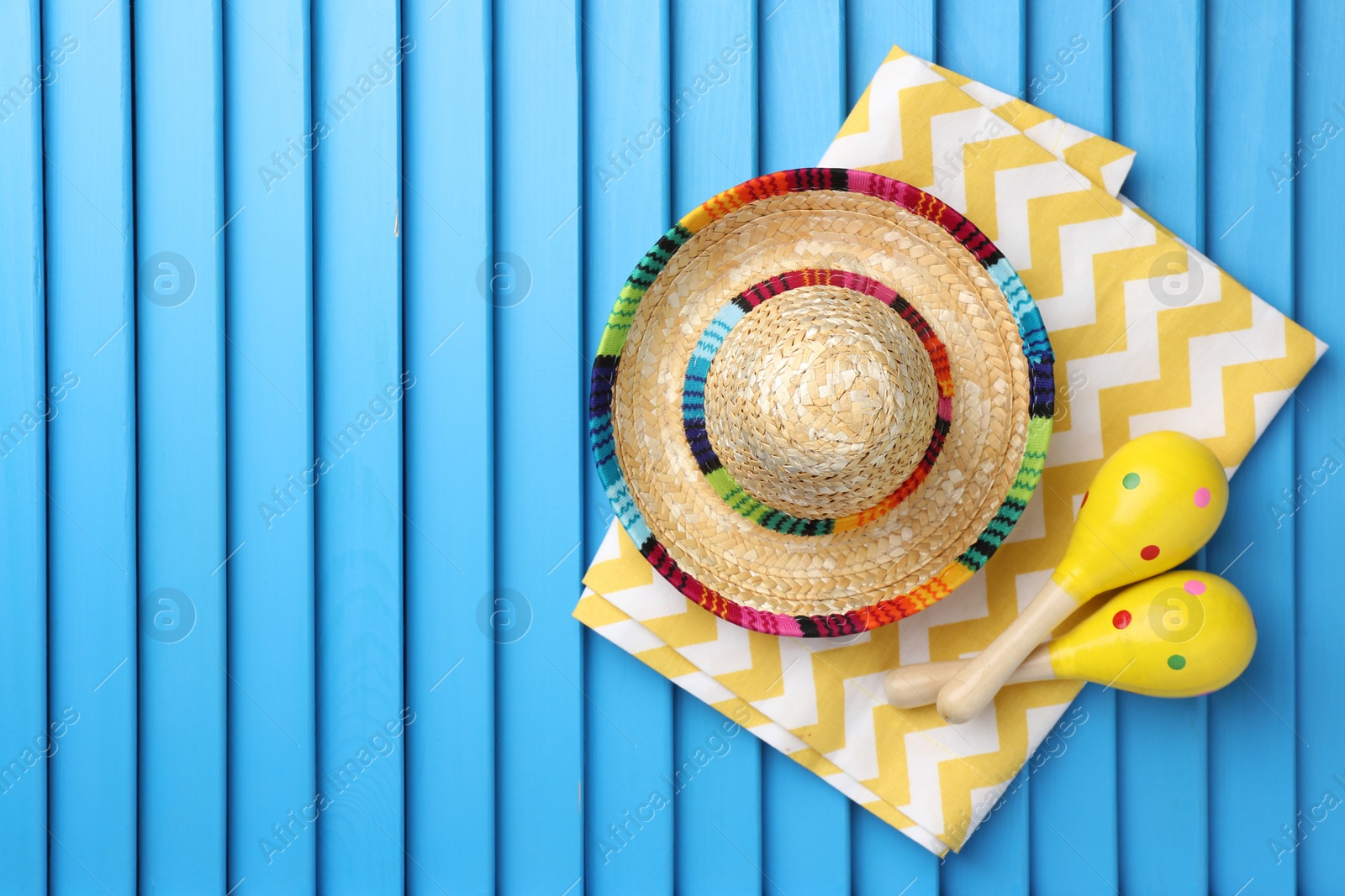 Photo of Mexican sombrero hat, towel and maracas on blue wooden surface, top view. Space for text