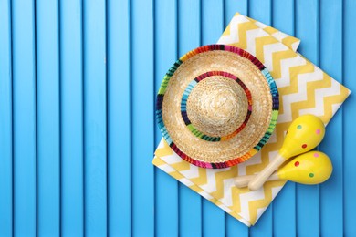 Photo of Mexican sombrero hat, towel and maracas on blue wooden surface, top view. Space for text