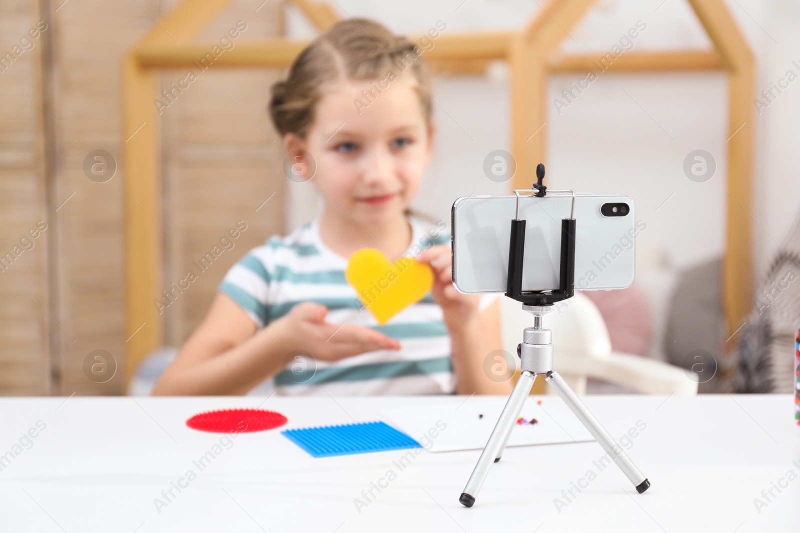 Photo of Cute little blogger with handcrafting recording video at home, focus on phone