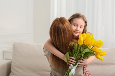 Photo of Daughter congratulating mom with bouquet of yellow tulips at home, space for text