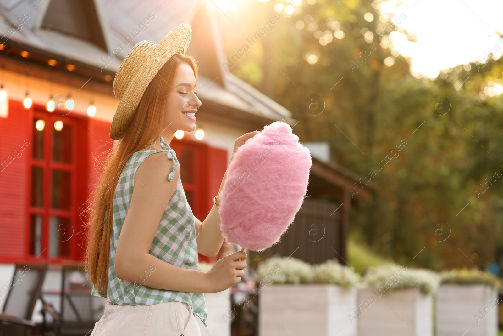 Photo of Smiling woman with cotton candy outdoors on sunny day. Space for text
