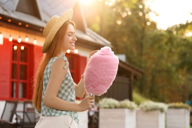 Photo of Smiling woman with cotton candy outdoors on sunny day. Space for text