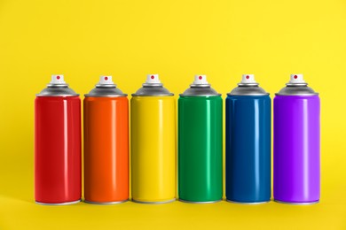 Colorful cans of spray paints on yellow background