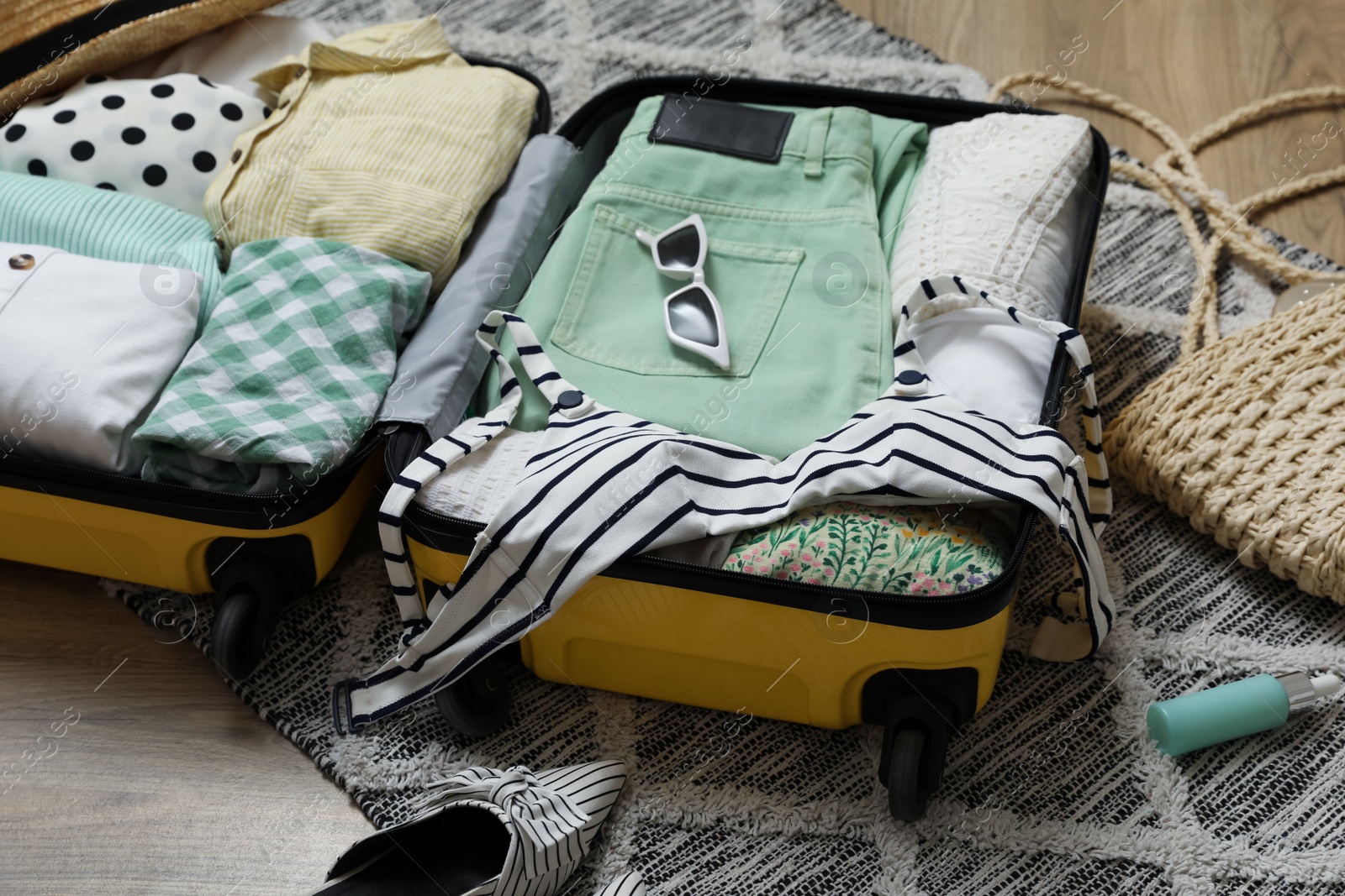 Photo of Open suitcase with summer clothes, accessories and shoes on floor