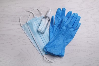 Protective masks, medical gloves and antiseptic on white wooden background, flat lay