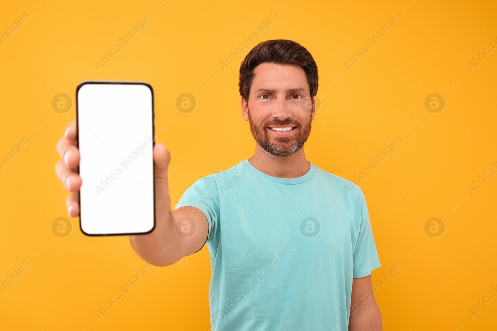 Photo of Handsome man showing smartphone in hand on yellow background