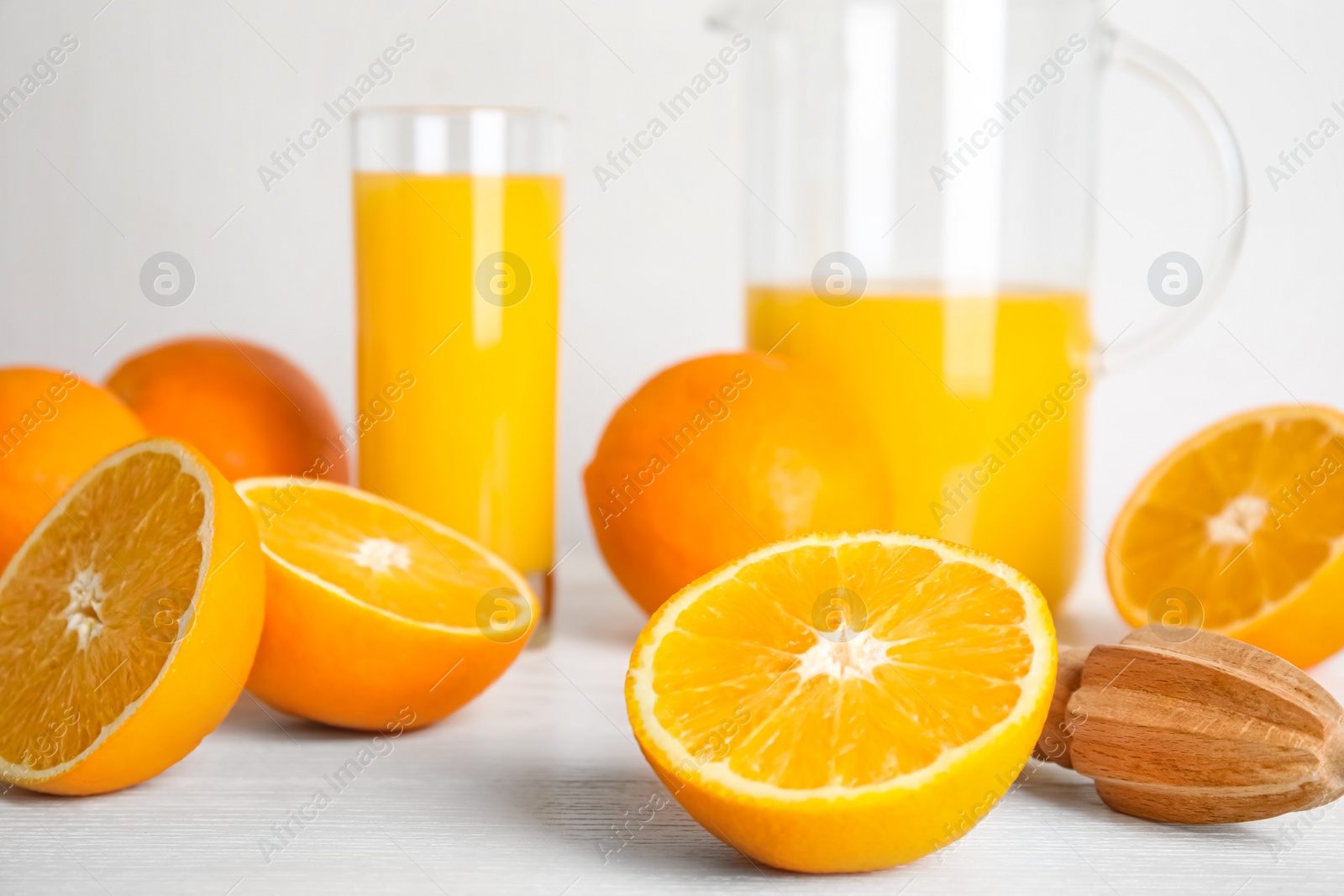 Photo of Fresh ripe oranges, juice and reamer on white wooden table