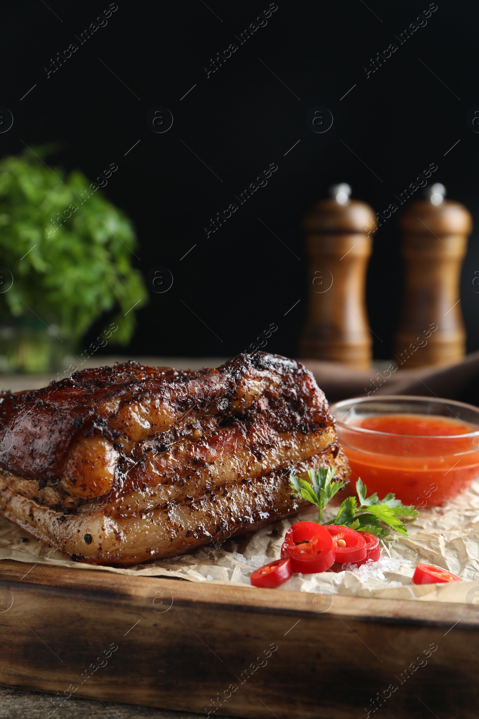 Photo of Piece of baked pork belly served with sauce and chili pepper on wooden board