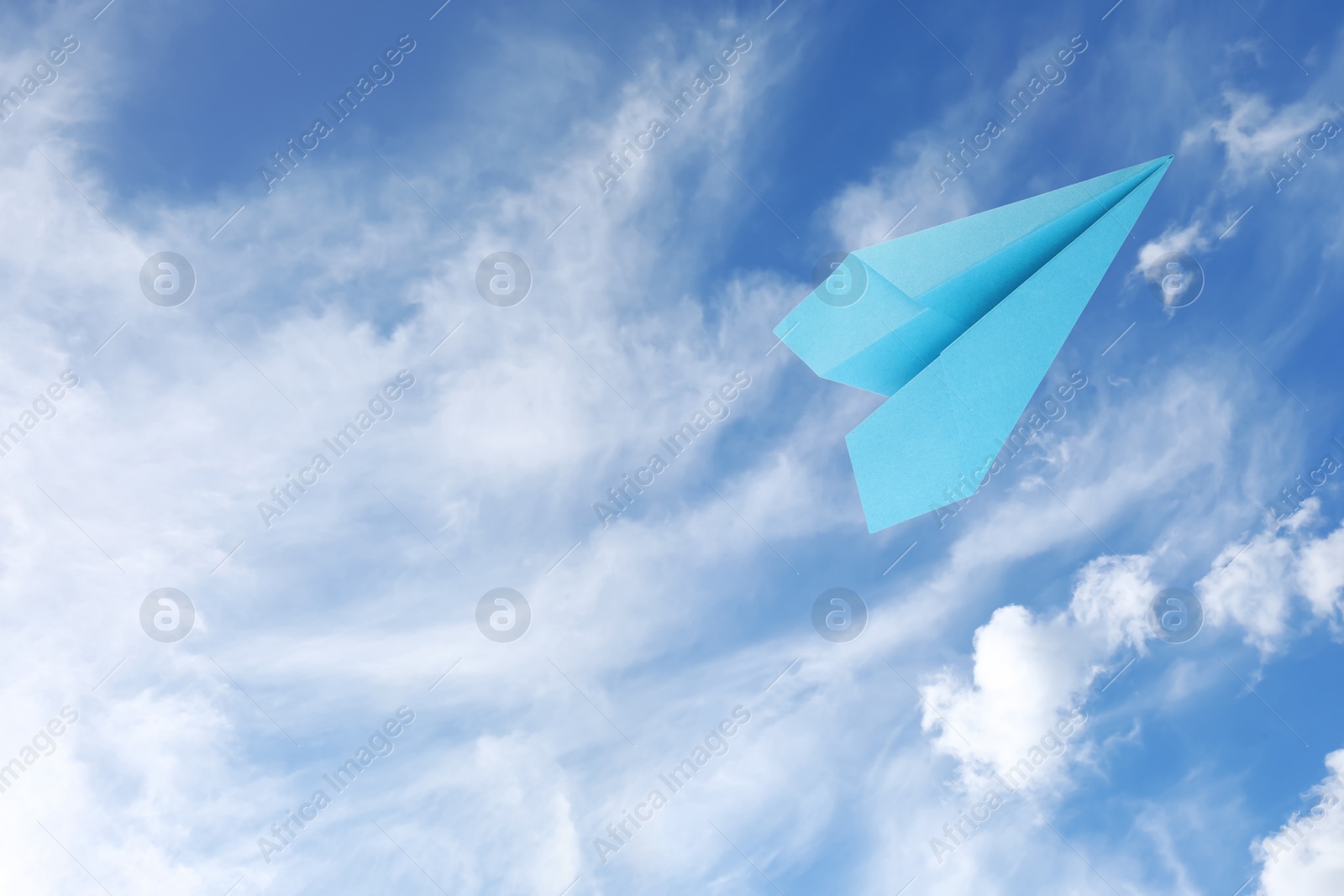 Image of Light blue paper plane flying in sky with clouds with clouds