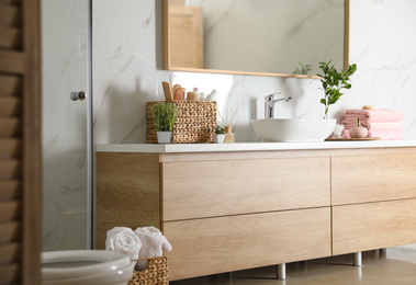 Photo of Elegant modern bathroom with wooden cabinet near marble wall