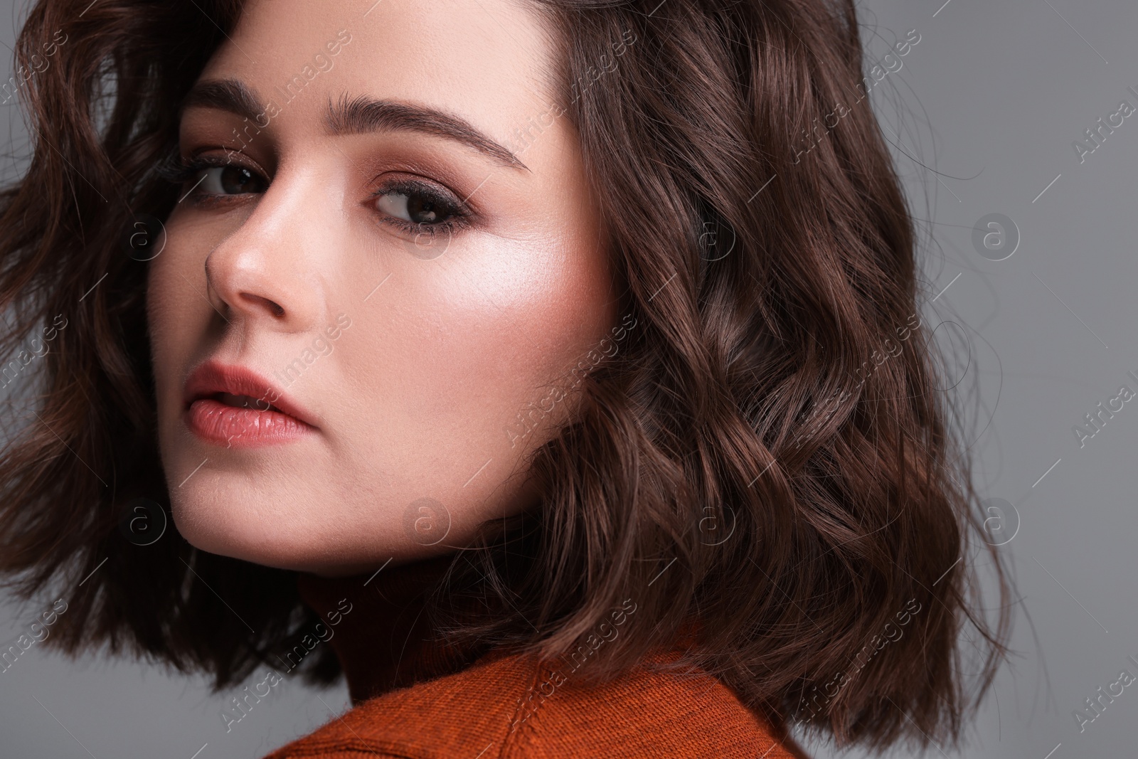 Photo of Beautiful young woman with wavy hairstyle on grey background, closeup