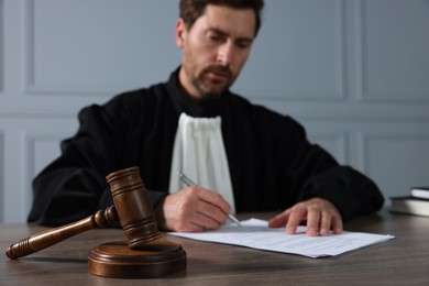 Photo of Judge with gavel writing in papers at wooden table indoors, selective focus