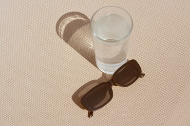 Photo of Stylish sunglasses and glass of water on grey surface, above view. Space for text