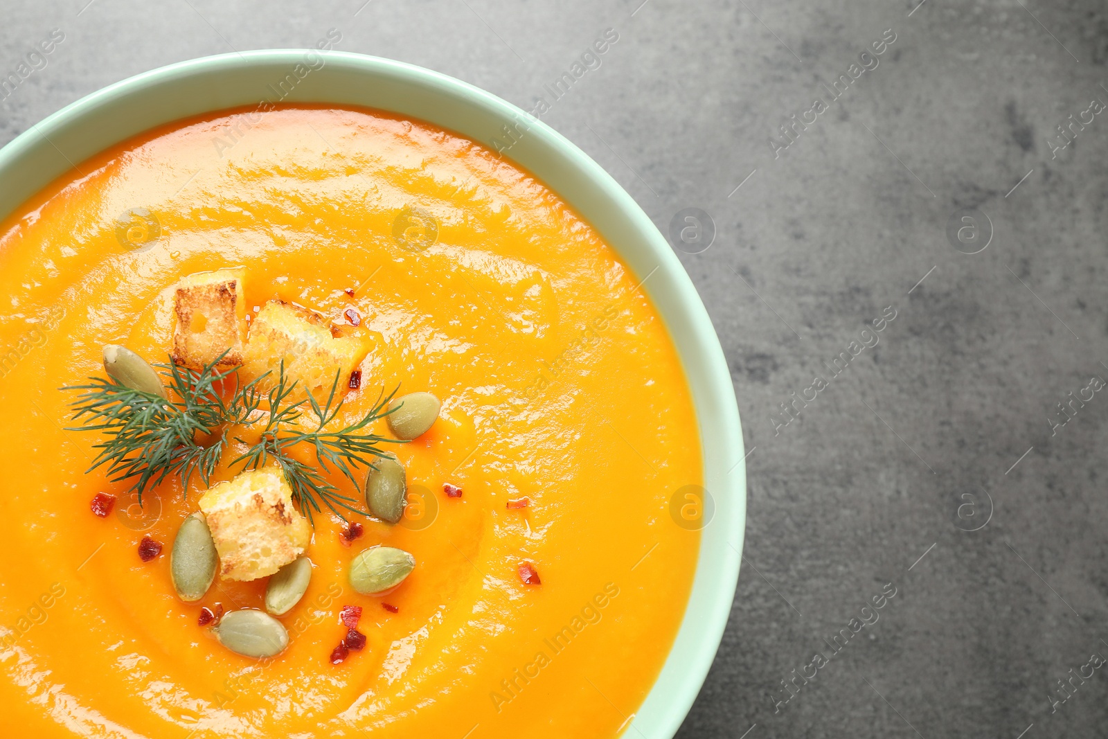 Photo of Delicious pumpkin soup in bowl on grey table, top view