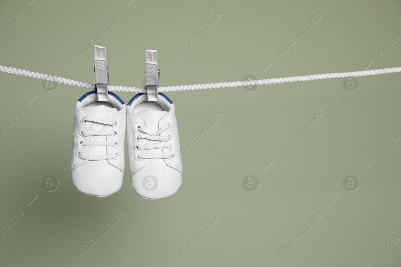 Photo of Cute small baby shoes hanging on washing line against green background, space for text