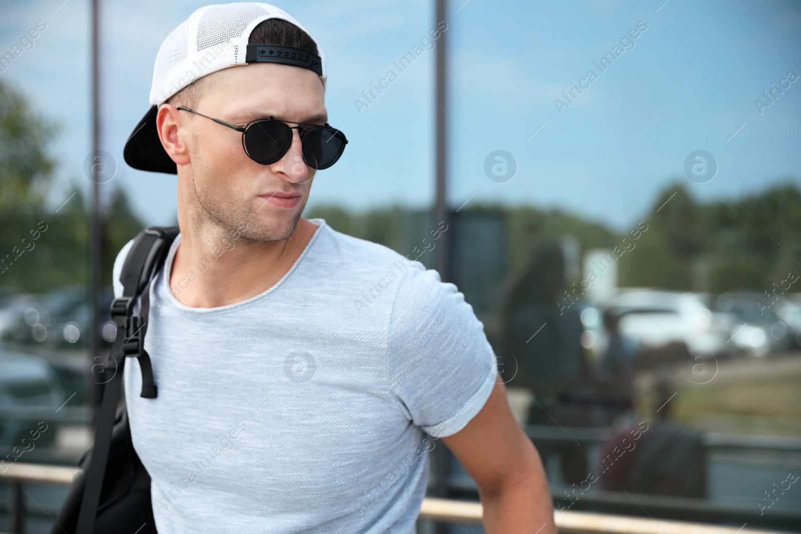 Photo of Handsome young man with stylish sunglasses and backpack near reflection surface outdoors, space for text