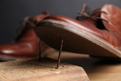 Photo of Metal nails in wooden plank and shoes on table, closeup