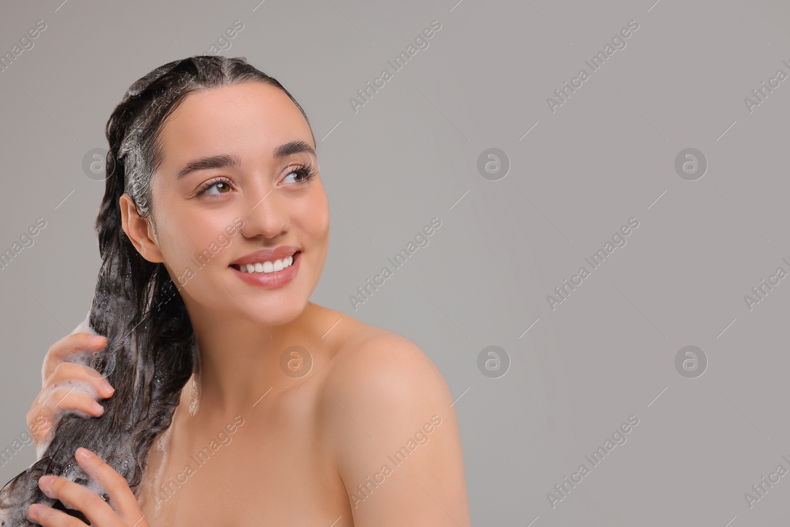 Photo of Beautiful happy woman washing hair on grey background. Space for text