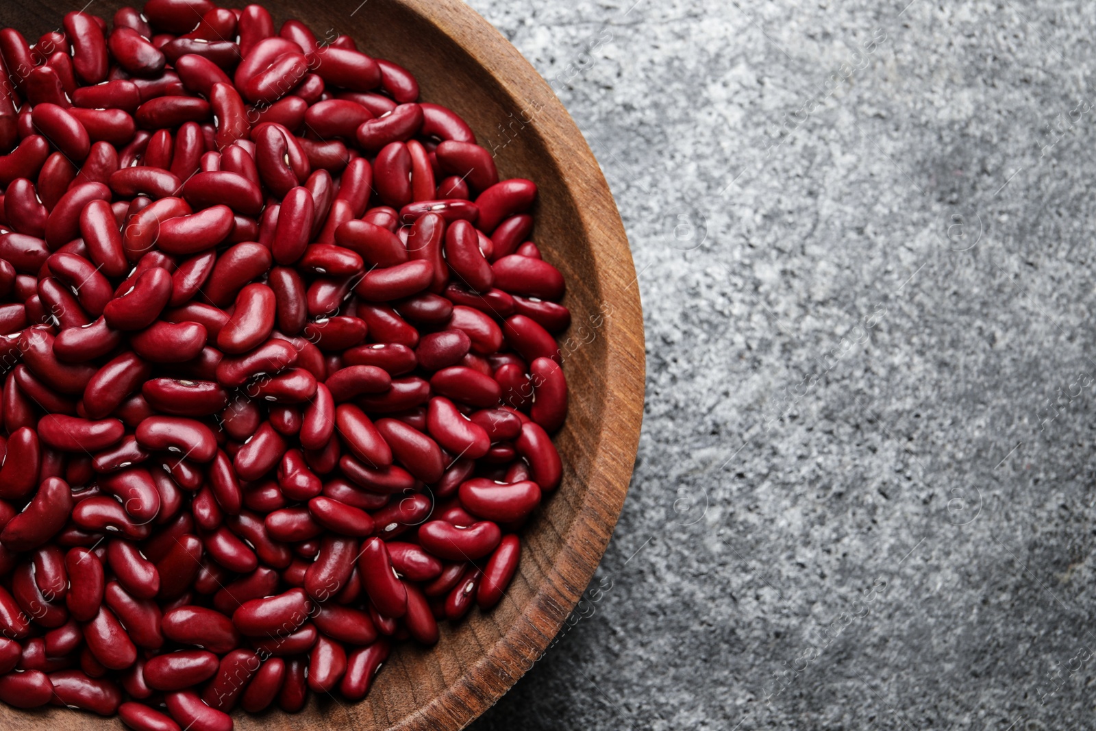 Photo of Raw red kidney beans in wooden bowl on grey table, top view. Space for text