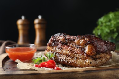 Photo of Piece of baked pork belly served with sauce and chili pepper on wooden board, closeup