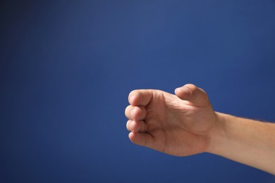 Photo of Man holding something in hand on blue background, closeup. Space for text