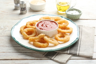 Photo of Plate with fried onion rings and sauce on table