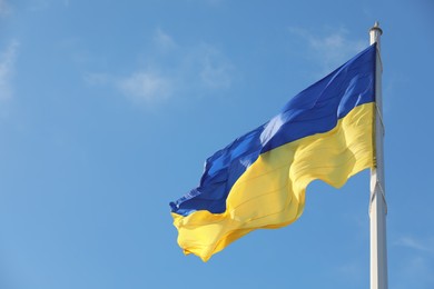 Photo of Flag of Ukraine waving on pole under blue sky. Space for text