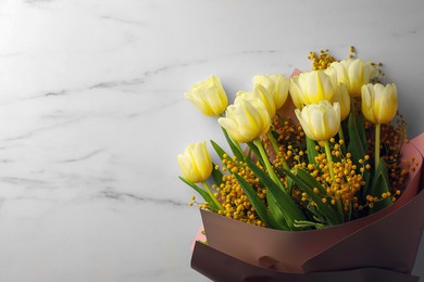 Bouquet with beautiful tulips and mimosa flowers on white marble table, top view. Space for text