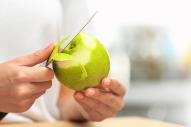 Photo of Woman peeling fresh green apple indoors, closeup. Space for text