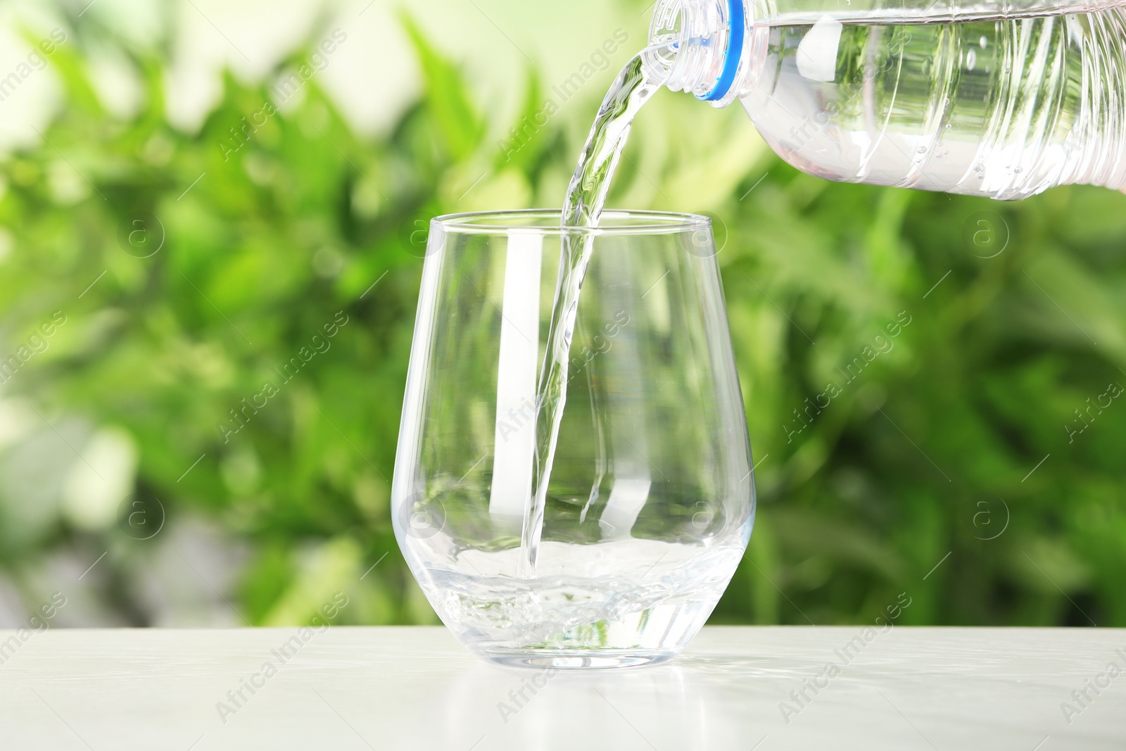Photo of Pouring water from bottle into glass on table against blurred background