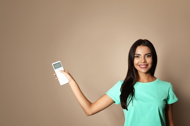 Photo of Young woman with air conditioner remote on beige background. Space for text