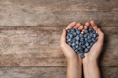 Photo of Woman holding juicy fresh blueberries on wooden table, top view. Space for text