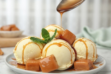 Photo of Pouring caramel sauce onto delicious ice cream served on table, closeup