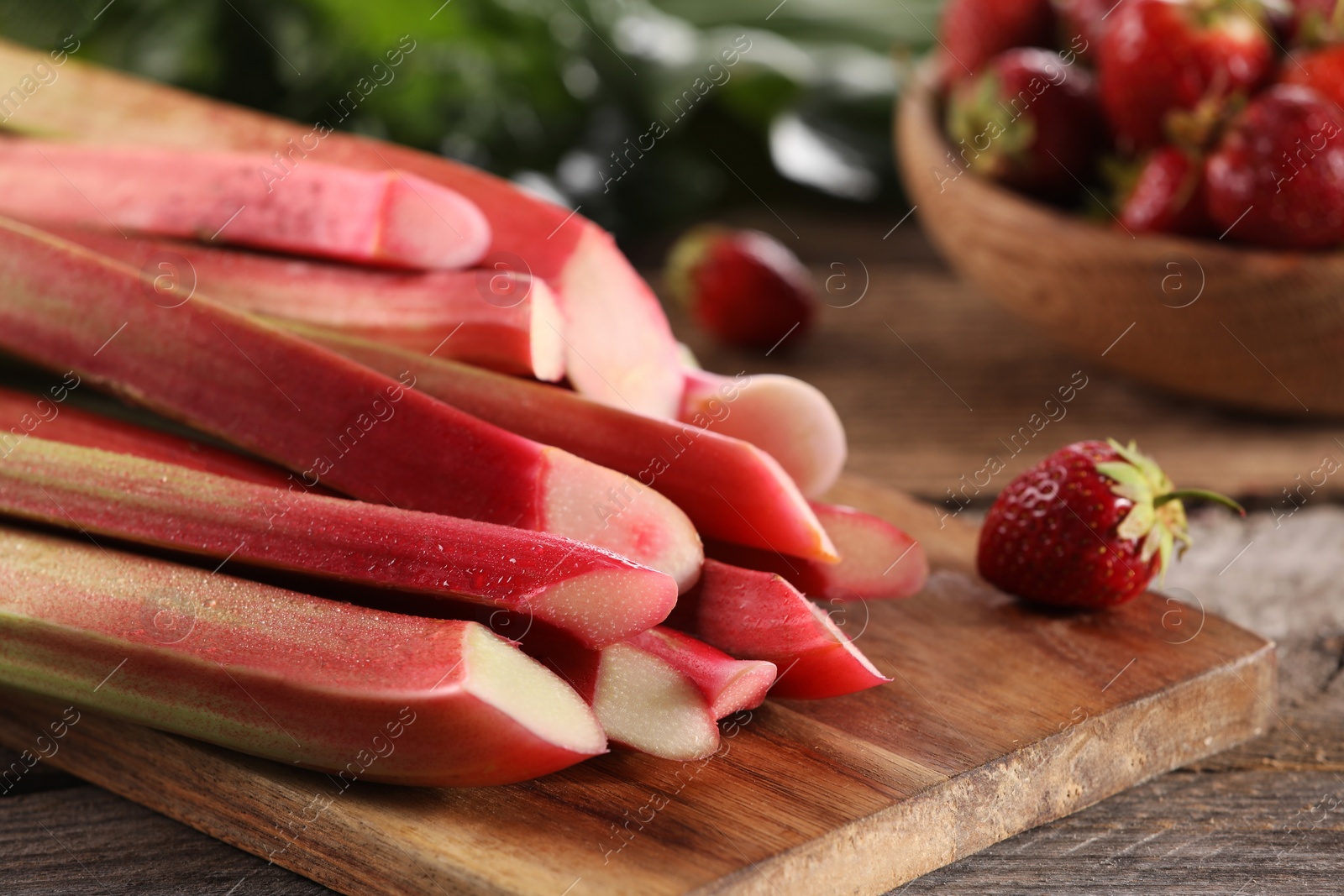 Photo of Cut fresh rhubarb stalks and strawberry on wooden table, closeup