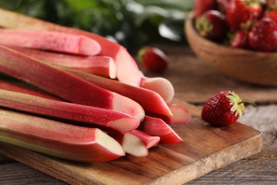 Cut fresh rhubarb stalks and strawberry on wooden table, closeup