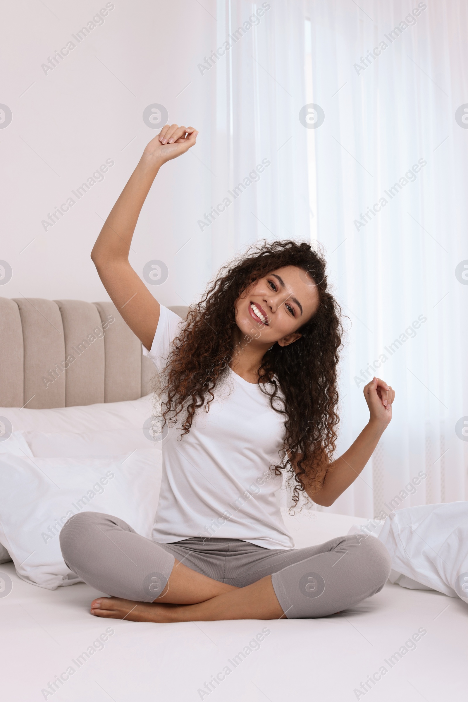 Photo of Happy African American woman stretching on bed at home