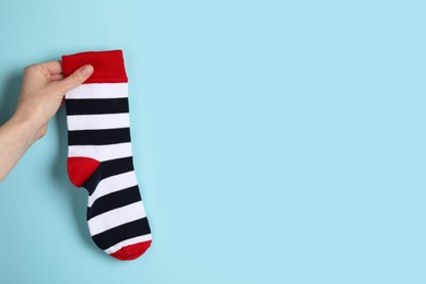 Photo of Woman holding striped sock on light blue background, closeup. Space for text