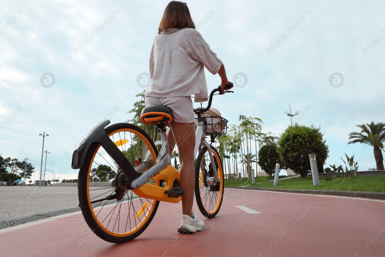 Photo of Young woman with bicycle on lane outdoors, back view