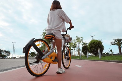 Young woman with bicycle on lane outdoors, back view