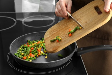 Photo of Woman putting tasty vegetable mix in frying pan at home, closeup