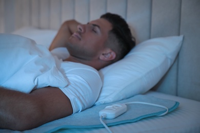 Photo of Man sleeping on electric heating pad in bed at night